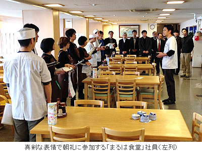 真剣な表情で朝礼に参加する「まるは食堂」社員(左列)